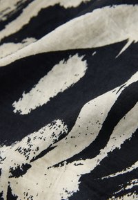 Motif abstrait noir et blanc sur tissu avec des formes irrégulières semblables à des coups de pinceau et une légère texture visible.