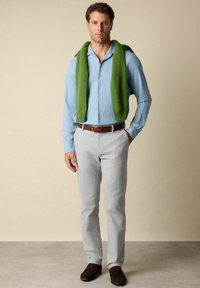 Lichtblauwe button-up shirt, groene gebreide trui over de schouders, grijze broek, donkerbruine schoenen. Eenvoudig ontwerp, zachte texturen.