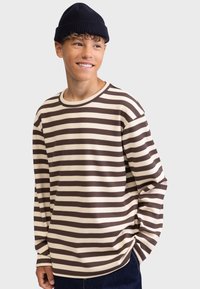 Vaffelsstrikket, langermet genser med rund hals i kremfarge med mørkebrune vannrette striper. Kombinert med en marineblå lue, med avslappet passform.