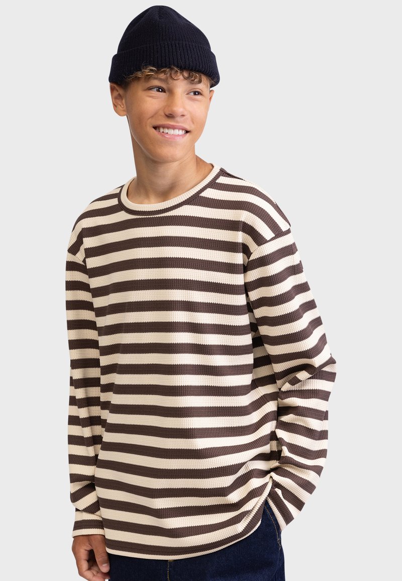 Vaffelsstrikket, langermet genser med rund hals i kremfarge med mørkebrune vannrette striper. Kombinert med en marineblå lue, med avslappet passform.