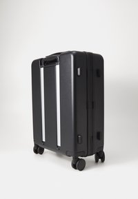 Black hard-shell suitcase with four wheels, two horizontal silver accents, a top handle, and a textured surface for grip.