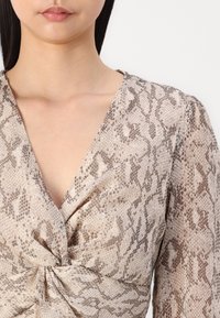 Top a maniche lunghe, stile avvolgente, di un beige chiaro con motivo a stampa di serpente. Presenta una scollatura a V e un dettaglio arricciato in vita.