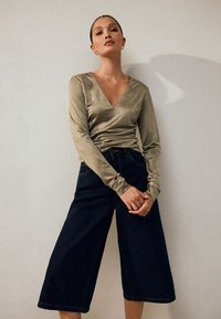 Zelta krāsas garroku krekls ar V-veida izgriezumu un savāktu detaļu, kopā ar tumši zila platām kājām džinsu kulotēm. Gluda tekstūra un ikdienišķs dizains.