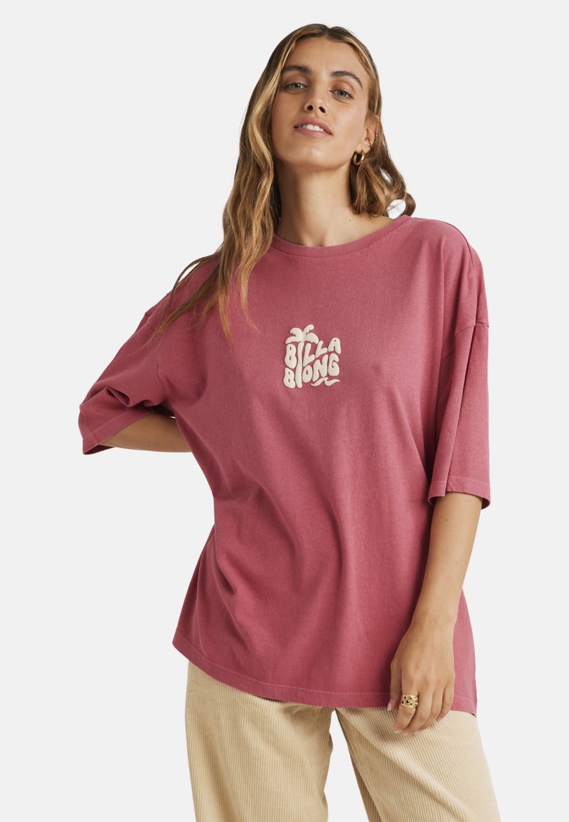 Oversized pink T-shirt with short sleeves and a crew neck, featuring a white, stylized "Billabong" logo on the front. Casual cotton fabric.