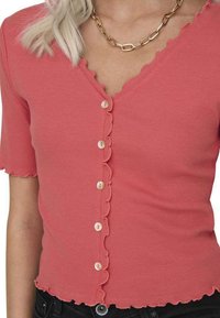 Haut en rose côtelé avec un décolleté en V, des manches courtes et un ourlet volanté. Il possède cinq boutons sur le devant et une silhouette ajustée.