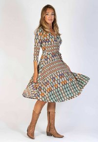 Mönstrad klänning med ett geometriskt tryck i nyanser av brunt, orange, grönt och blått; tillverkad av lättviktsmaterial med trekvartsärmar och en midjeband.