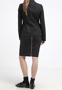 Svart skräddarsydd blazer med en elegant design, kombinerad med en knälång svart kjol med gulddetalj i dragkedjan bak.