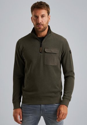 Olijfgroen pullover met hoge kraag, ritskraag, voorzak, geribbeld textuur en lange mouwen, gecombineerd met blauwe jeans.