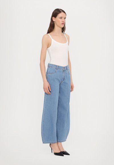 Light blue wide-leg jeans with a high waist, paired with a fitted white tank top and black pointed-toe heels. Smooth denim texture.