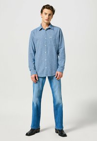 Camicia a quadri blu con colletto button-down, maniche lunghe e taschino; abbinata a jeans azzurri chiari e stivaletti neri con tacco.