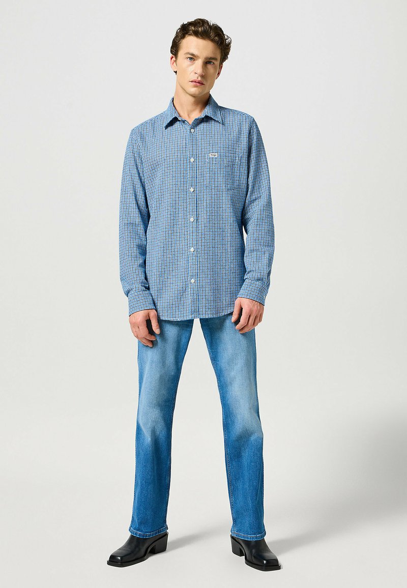 Camicia a quadri blu con colletto button-down, maniche lunghe e taschino; abbinata a jeans azzurri chiari e stivaletti neri con tacco.