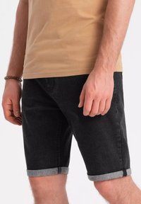 Pantalones cortos de mezclilla negros con dobladillos enrollados, que presentan una textura suave y un diseño ajustado. Combinados con una camiseta de manga corta beige.