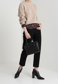 Beige rippad tröja, blommönstrad skjorta under, svarta byxor, spetsiga svarta ankelskor, håller en liten svart handväska.