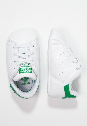Hvide Adidas Stan Smith børnesko med grøn hælkappe og logo, en sko set ovenfra, en sko set fra siden på hvid baggrund.