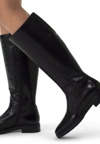 Black knee-high boots made of smooth leather, featuring a tight fit, side zipper, and flat sole for stability. Simple, sleek design.