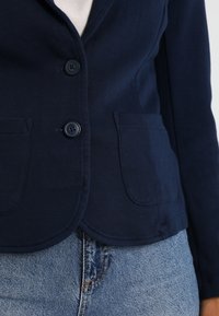 Marinblå blazer med en texturerad tyg, två framfickor och knäppning. En klassisk design med en skräddarsydd passform, i kombination med ljus denim.