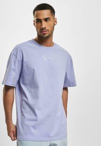 Lyserød bomulds t-shirt med rund hals og korte ærmer, der har et hvidt signaturlogo trykt på brystet.