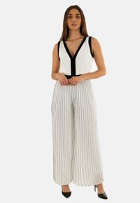 Mono sin mangas de color blanco con un escote negro y rayas verticales negras. Presenta piernas de pantalón anchas y fluidas, además de tacones de aguja.