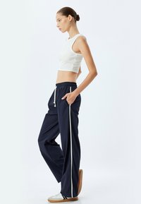Hvid ribbet crop top parret med marineblå bukser med snor i taljen, der har sidestriber, lommer og en afslappet pasform. Hvide og beige sneakers fuldender looket.