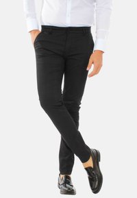 Pantaloni neri su misura con una trama testurizzata, vestibilità slim e tasche laterali, abbinati a mocassini neri lucidi e una camicia bianca con bottoni.