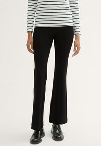 Black flared trousers with a smooth texture, high waist, and side seams. Paired with a striped long-sleeve top and black shoes.