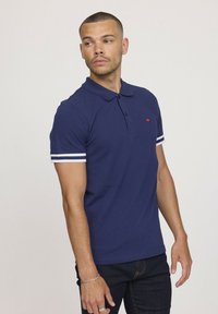 Polo bleu marine avec des manches courtes à rayures blanches, deux boutons au col et un petit logo rouge sur la poitrine. Design à coupe classique.