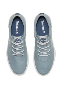 Baskets en toile bleu clair avec lacets blancs, bout arrondi et semelle en caoutchouc blanc. Logo Timberland et emblème arbre sur le côté et la languette.