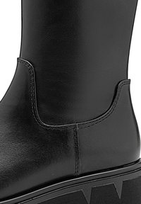 Black leather ankle boot with a smooth texture, featuring stitch detailing and a thick wedge sole with a zigzag pattern on the edge.