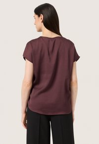 Burgundy texturovaný krátký rukáv top s kulatým výstřihem, který má volný střih a zakřivený lem, v kombinaci s černými kalhotami.