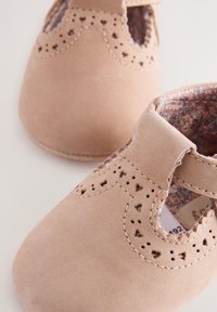 Chaussures souples rose pâle pour tout-petits avec des perforations en forme de cœur et une bride sur le cou-de-pied, montrant une doublure intérieure à motif floral.