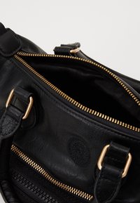 Zwarte leren handtas met gouden rits, interieurvoering en opvallende stiksels. Voorzien van dubbele riemen en een geperst circulair detail.