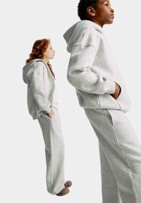 Grå fleece hættetrøje og sweatpants sæt med afslappet pasform, sidelommer og en blød tekstur, båret med brune træskoser.