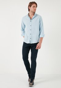 Camisa de botones azul claro, de mangas largas recogidas en los puños, con botones negros, combinada con jeans azul oscuro y zapatillas grises.