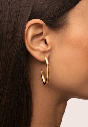 Boucle d'oreille en or avec une surface lisse et polie, de forme courbée et allongée. Portée sur le lobe de l'oreille, elle présente un design épuré.