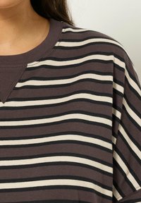 T-shirt marron à rayures avec des rayures horizontales crème et noires, col rond et manches courtes, fabriqué en coton doux.