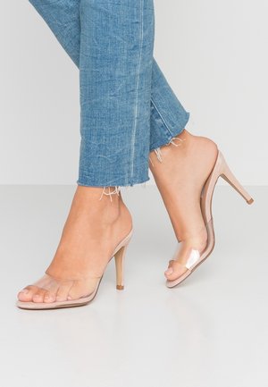Gennemsigtige hæle sandaler i nude farve, med en gennemsigtig rem over tæerne, åben ryg og et elegant højhælet design.