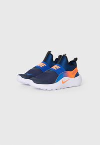 Une paire de baskets Nike bleu marine sans lacets avec des accents orange et bleu, des semelles blanches et "Just Do It" sur la sangle latérale.