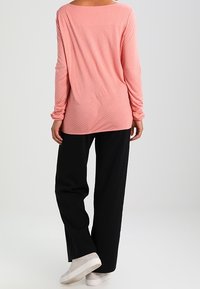 Långärmad rosa topp med prickar, lös passform, rundad halsringning, tillsammans med svarta vida byxor och ljusgrå sneakers.