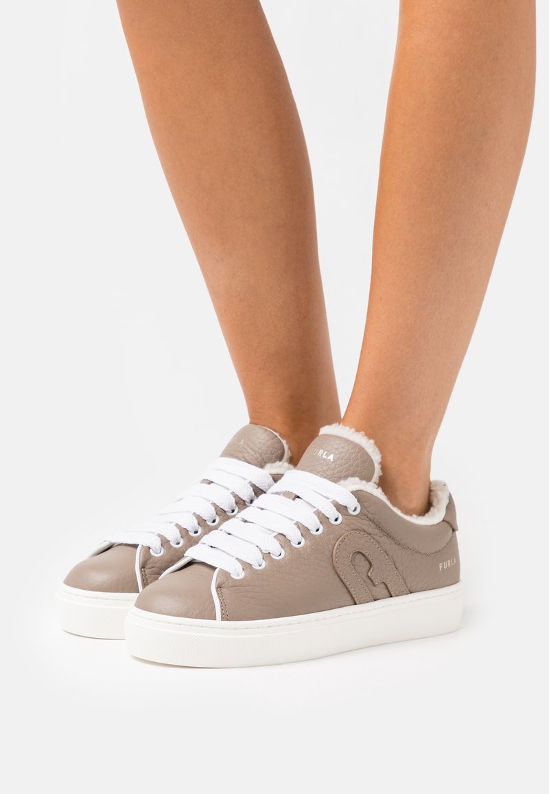 Baskets en cuir taupe avec lacets blancs et doublure en polaire portées aux pieds sur un fond blanc uni.