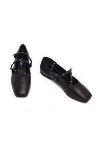 Ballerine in pelle nera con punta quadrata, caratterizzate da cinturini decorativi con borchie che si incrociano sul collo del piede e un tacco basso per una maggiore stabilità.