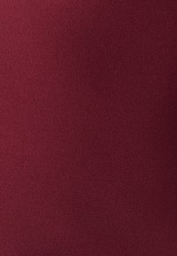 Burgundijska tkanina s glatkom, mat texturom. Površina je ujednačena, bez uzoraka ili vidljivih šavova, nudeći izgled čvrste boje.