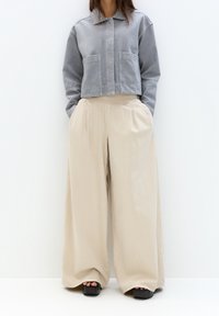 Giacca di jeans grigia corta con due tasche frontali abbinata a pantaloni beige a gamba larga. Tessuto strutturato e vestibilità ampia in colori neutri.