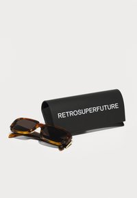 Gafas de sol de carey marrón con lentes oscuros, acompañadas de un estuche rígido negro que presenta en blanco el texto: "RETROSUPERFUTURE."