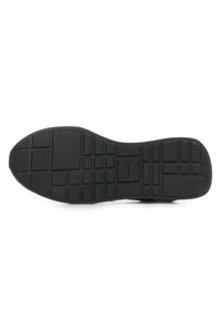 Suela de zapato de goma negra con un patrón texturizado que presenta formas rectangulares y cuadradas para mejorar la agarre y la durabilidad, con el logo de "Calvin Klein" en relieve.