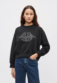 Μαύρο φούτερ με κομψή κομμένη σχεδίαση, στρογγυλή λαιμόκοψη και υπερμεγέθη μανίκια. Διαθέτει λευκό γραφικό χείλους με το κείμενο "Pepe Jeans London".