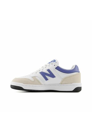 Baskets basses blanches avec bout en suède beige, accents bleus, logo "N" bleu et semelle noire sur fond blanc.