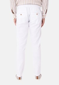 Pantaloni bianchi in lino con cintura elastica, dotati di due tasche posteriori con chiusura a bottone. Tessuto testurizzato e design affusolato.