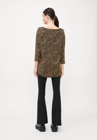 Fekete és arany zebramintás felső, háromnegyedes ujjakkal, fekete bővülő nadrággal és tömzsi fekete lábbelivel párosítva. Simas texture.