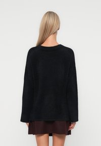 Pull noir en tricot pelucheux avec un col rond, des épaules tombantes et des manches longues, associé à une jupe bordeaux. Pas de motifs ni de matériels visibles.