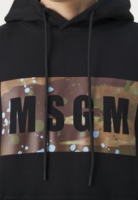 Czarna bluza z kapturem z dużą brązową grafiką z wzorami rozprysków oraz wyraźnym czarnym napisem "MSGM". Projekt dopełniają sznurki regulacyjne.